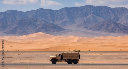 Tan Military Truck Driving on a Desert Road with Sand Dunes and Mountains