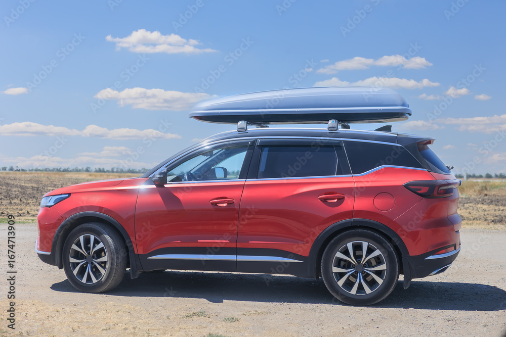 Fototapeta premium Red SUV on a country road against a cloudy sky, close-up