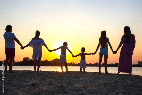Family gathered at the beach holding hands as the sun sets over the water in summer