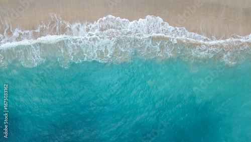 Aerial view of turquoise sea waves crashing on sandy beach creating natural abstract pattern