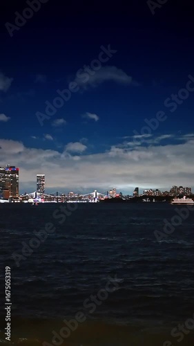 Boat travel by the dark river at rainy evening. Luminous skyline of New York at backdrop. Vertical video.