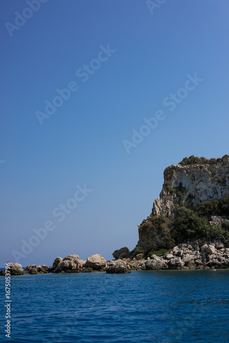 Rocky land in the sea on sunny day and blue sky. Blue water and bright summer view.
