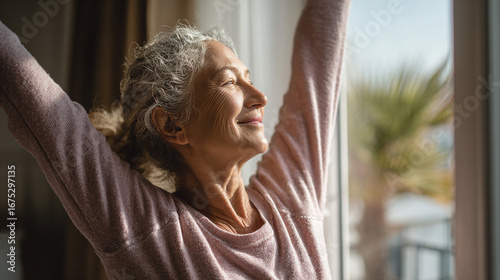 Elderly woman doing light stretching exercise at home, smiling, healthy lifestyle, sunlight through window.
