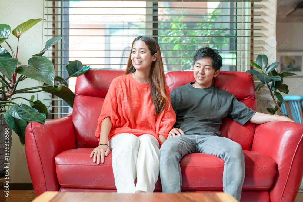Obraz premium A man and woman are sitting on a red couch. The woman is wearing an orange shirt. Scene is warm and friendly