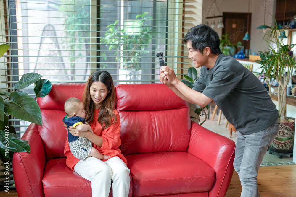 Obraz premium A man is taking a picture of a woman and a baby on a red couch. Scene is warm and loving, as the family is spending quality time together