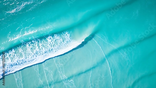 Aerial view of turquoise waves meeting white sand, creating abstract patterns under morning sunlight.