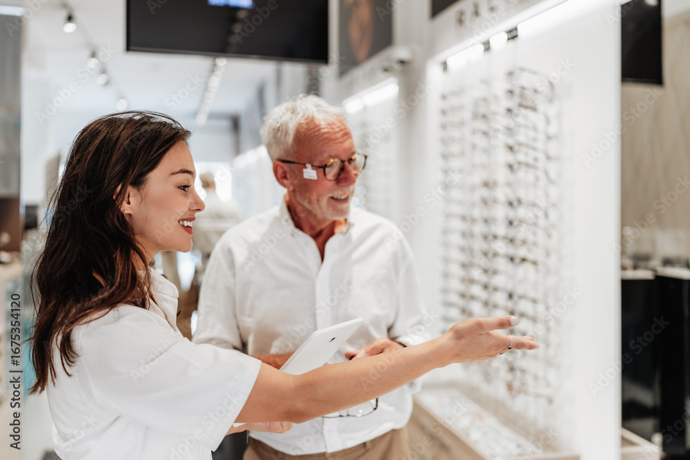 Obraz premium Smiling female optician assisting a senior man choosing new eyeglasses in a modern optical store, providing professional advice and personalized service.