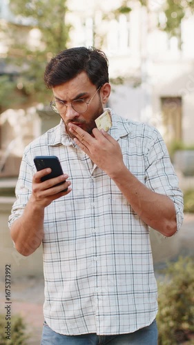Shocked Indian man trying to pay online shopping with smartphone blocked credit card. Annoyed young Hispanic tourist on street buying bank refuse problem unsuccessful payment lack of money balance.