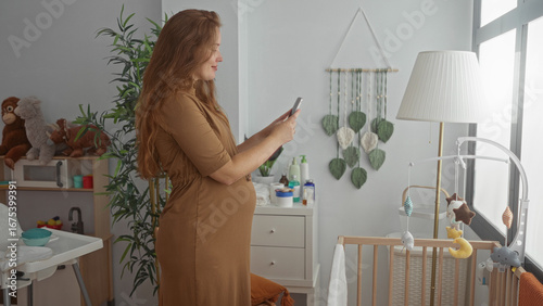 Фотография Pregnant woman stands in a softly lit bedroom texting on smartphone while gently cradling her bare belly; maternal serenity