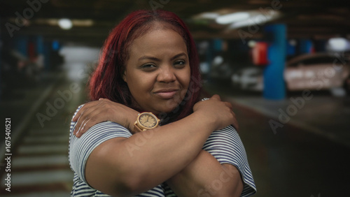 Konstfotografi Woman wearing wooden watch hugs shoulders with crossed arms inside a parking building; self care reflection