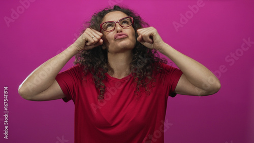 Billede på lærred Hispanic woman wearing red shirt wipes tears from cheeks in studio; sadness sorrow grief vulnerability