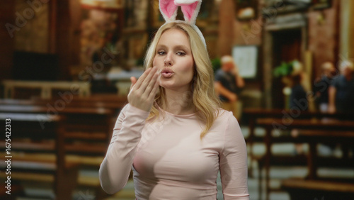 Wallpaper Mural Blonde woman with bunny ears sending a kiss while standing in a catholic church, blending humor and tradition in a unique and playful setting. Torontodigital.ca