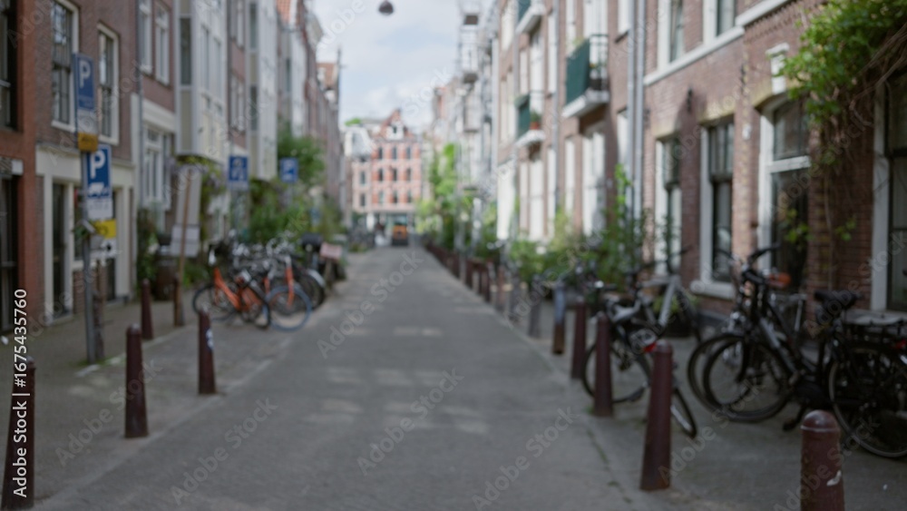 Obraz premium Blurry urban street scene in amsterdam with bicycles lining the narrow alleyway, showcasing the classic european architecture typical of the netherlands in a defocused view.