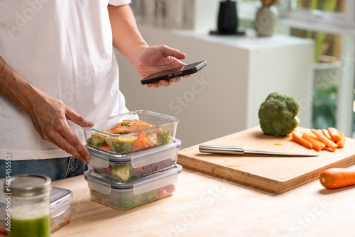 Person using smartphone app for calorie counting and photo sharing above homemade weight loss meal prep.