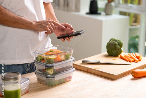 Person using smartphone app for calorie counting and photo sharing above homemade weight loss meal prep.