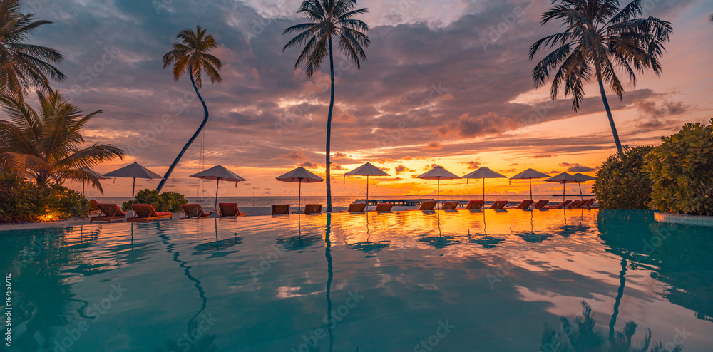 Obraz premium Luxury summer travel resort with peaceful swimming pool, palm trees, lounge chairs and umbrellas, relaxing reflections in water, amazing vacation scenery, perfect sunset landscape for tropical getaway