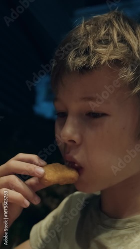 Close-up of a boy eating nuggets. Teen boy eats in fast food. Soft evening lighting and blurred background create a warm, cozy, and candid moment. The concept of tasty but unhealthy food for children