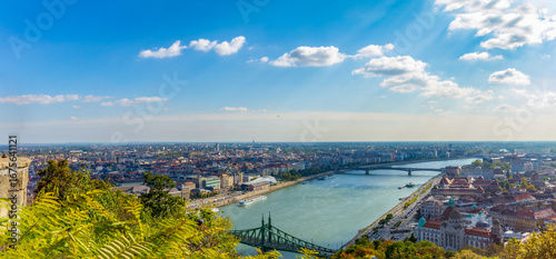 Bilde på lerret Panoramic view from Gellert Hill lookout showing blue Danube River, green Liberty Bridge, and city stretching to horizon under sunny blue sky