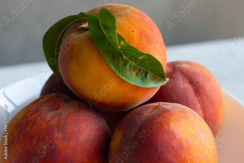 Fresh peaches with vibrant orange and yellow hues, nestled together in a white bowl, showcasing their natural beauty and lush green leaves for a healthy lifestyle concept