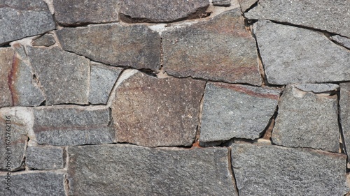 A close-up of a wall constructed from natural stones of varying shapes and sizes, highlighting its rough and uneven texture.