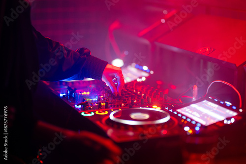 Tableau sur toile DJ adjusting mixer controls on an illuminated club deck bathed in red and blue stage lights