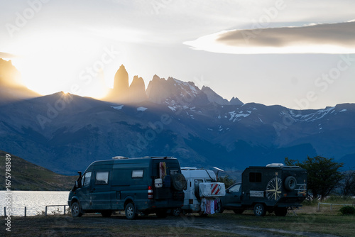 A group of friends in camper vans camp by a Patagonian lake, with the stunning Torres del Paine mountains at sunset. A celebration of adventure and community
