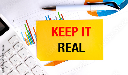 Keep it real phrase on yellow card with colorful charts, pen and calculator on white office background
