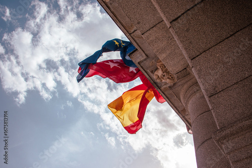 Low angle view of European, Spanish, and Community of Madrid Flags Waving at Plaza Mayor, Madrid, Spain