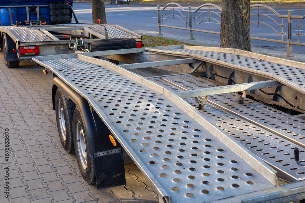 Obraz premium A heavy-duty car hauler sits parked on a city street, displaying its metal ramps and wheels under the afternoon sunlight