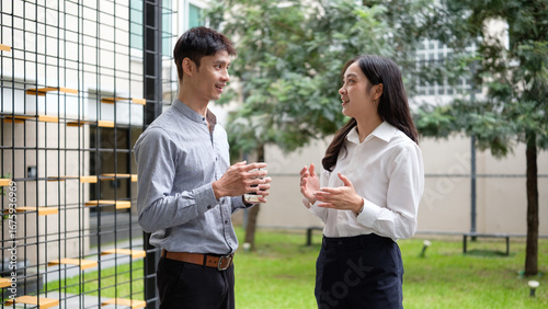 Young entrepreneurs discussing work casually during an outdoor break, with greenery and a modern office backdrop.