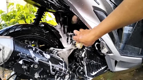 A hand is rubbing or washing a motorcycle with a sponge and soap.