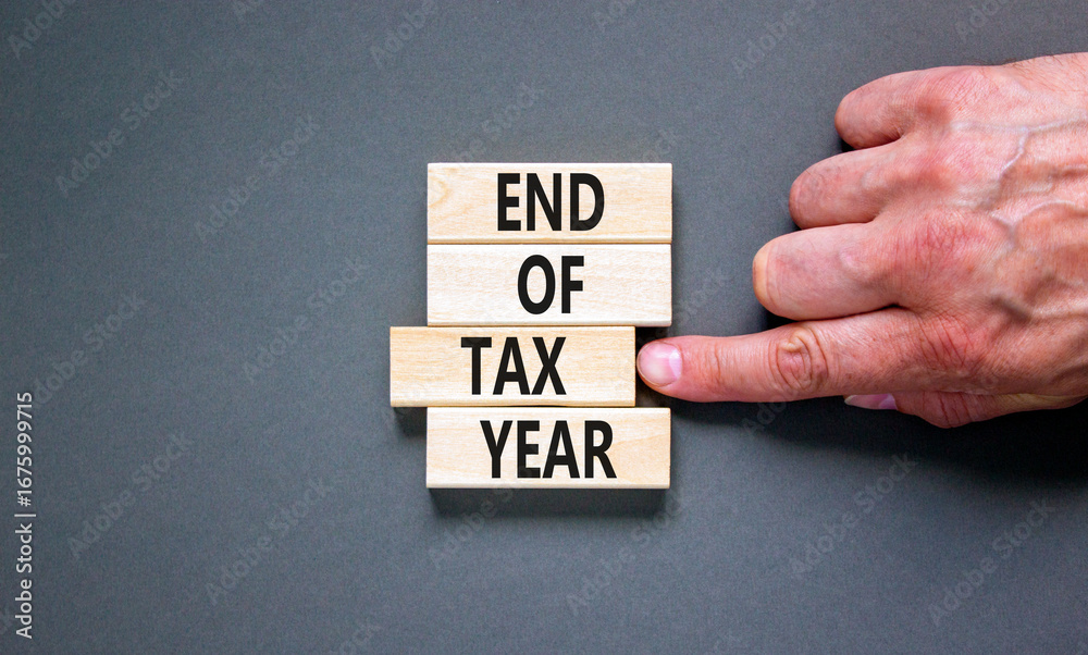End of tax year symbol. Concept words phrase End of tax year on beautiful wooden blocks. Beautiful grey paper background. Businessman's hand. Business End of tax year concept. Copy space. End of tax year symbol. Concept words phrase End of tax year on beautiful wooden blocks. Beautiful grey paper background. Businessman's hand. Business End of tax year concept. Copy space.