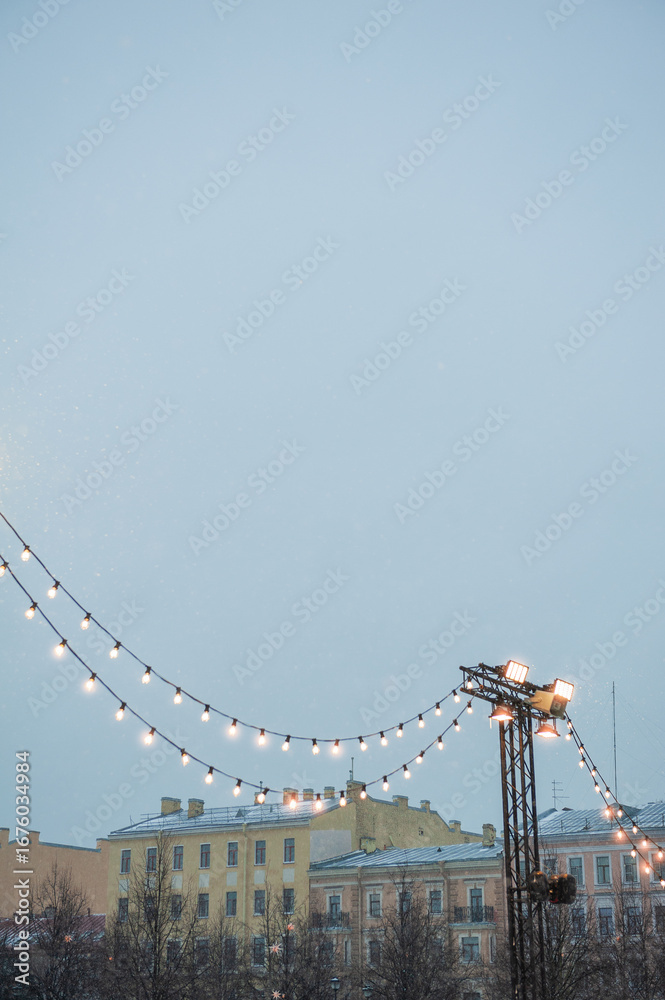 Fototapeta premium Festive string lights glow against historic city buildings