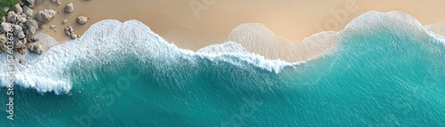 Aerial view of turquoise waves crashing onto a sandy beach with rocks on the shore.