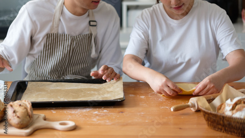 Close-up of hands shaping pastry dough with a baking tray and fresh bread in a homey kitchen setup.