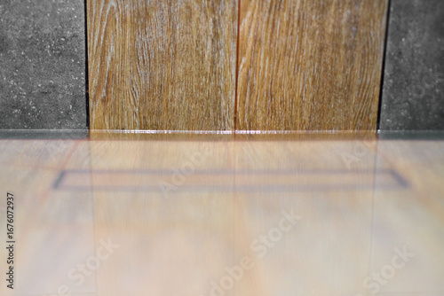 Minimalist shower floor featuring discreet drain embedded in wooden-style tiles. Gentle lighting highlights sleek design. Calm, neutral tones create serene atmosphere