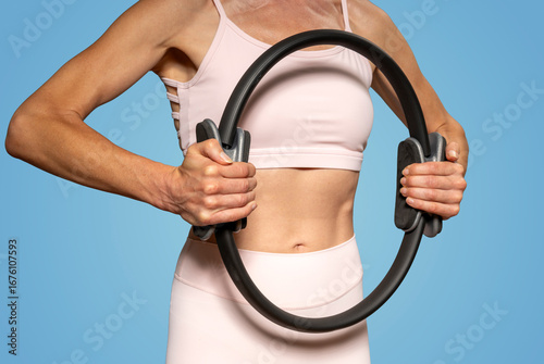A fit woman holding a pilates ring in her hands, wearing pink sports clothing.