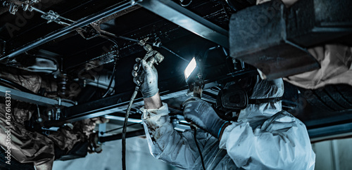 Automotive technician applying rustproof protective coating under a vehicle. Process helps prevent corrosion and extend vehicle lifespan. Ideal for illustrating car maintenance, vehicle care.