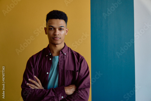 Portrait of confident young businessman standing arms crossed against colorful wall in office