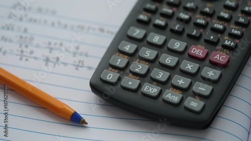 A scientific calculator and ballpoint pen lying on an open notebook with equations inside. Close up.
