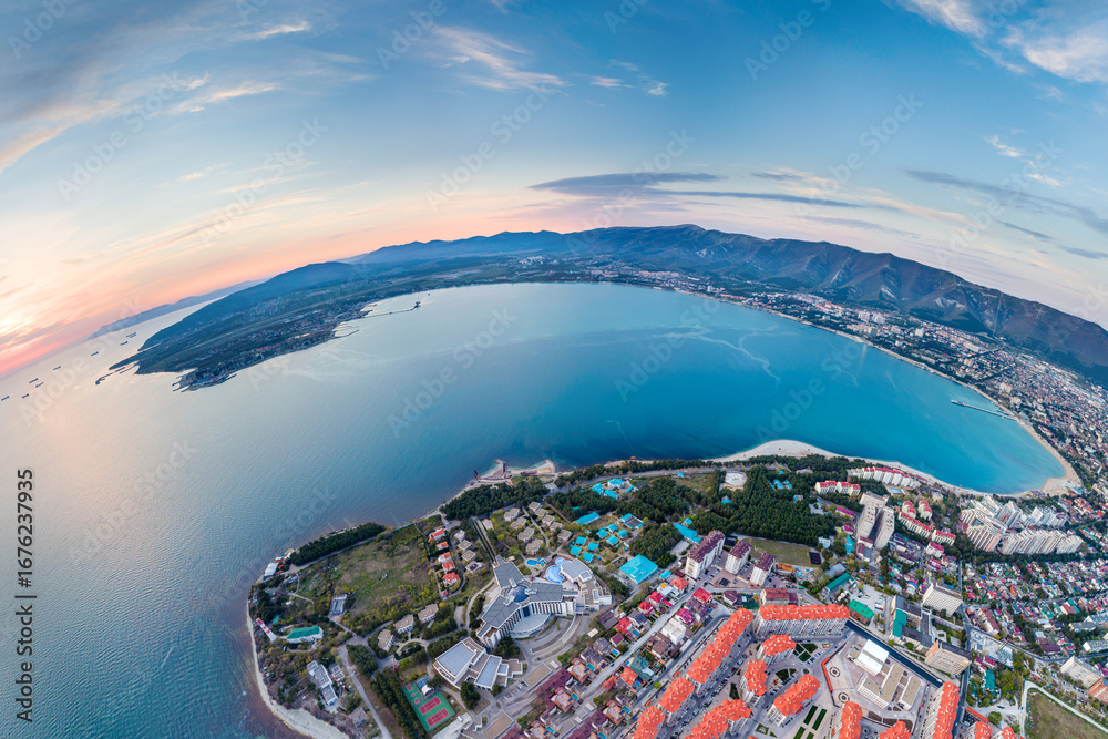 Fototapeta premium Panorama of Gelendzhik resort. Sunset. Gelendzhik Lighthouse on Kurtom Rocky Shore. Geleknji Bay and Caucasus Mountains in background. Aerial view.