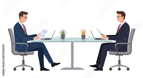 Two businessmen in suits seated at a table, working with laptops and documents, facing each other.