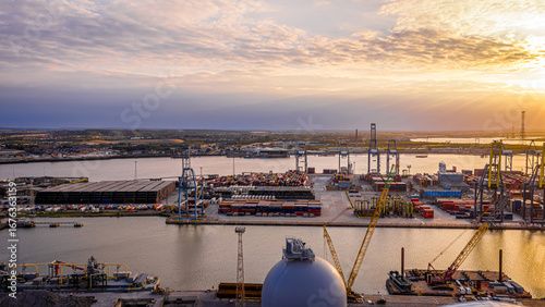 Cuadro en lienzo Golden hour drone shot of the busy Port of London, highlighting industrial activity, cranes, and shipping containers by the River Thames