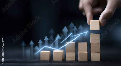 Image shows hand placing wooden block stack of blocks, with digital graph and upward arrows indicating growth and progress, symbolizing business
