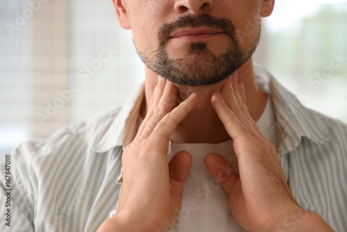Handsome man self-examining thyroid gland at home, closeup