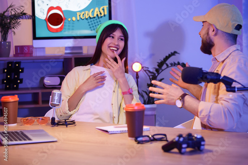 Young podcasters laughing at table in recording studio