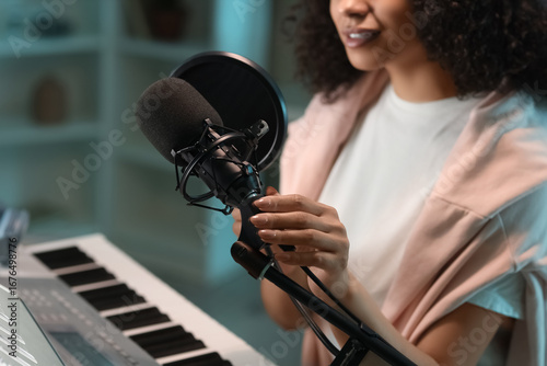 Фотография Young woman with microphone singing in recording studio, closeup