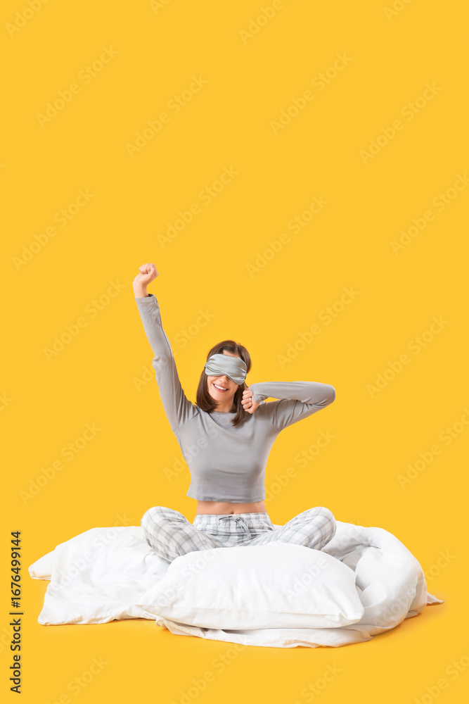 Fototapeta premium Young woman in pajamas sitting on blanket against yellow background