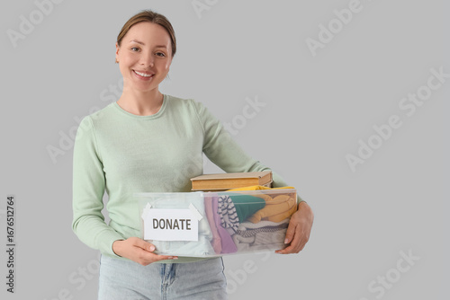 Young woman with container of clothes for donation on light background