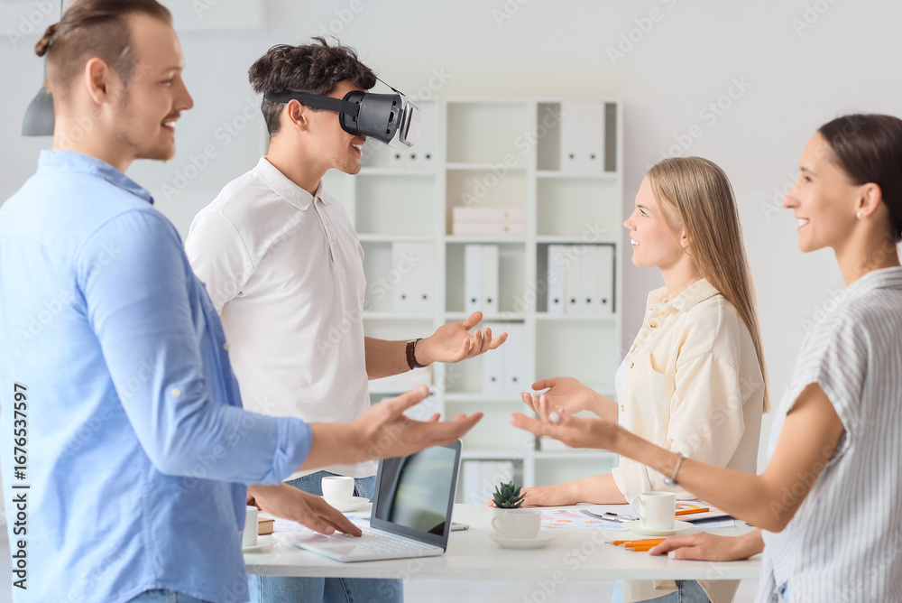 Fototapeta premium Young man using VR glasses with his colleagues in office